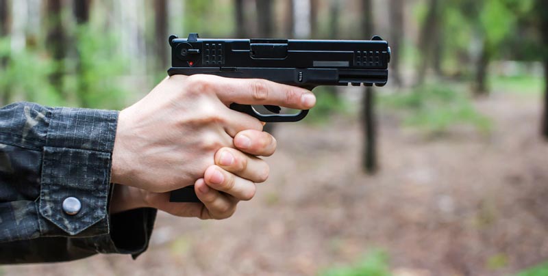 A modern pistol is fired in the woods.